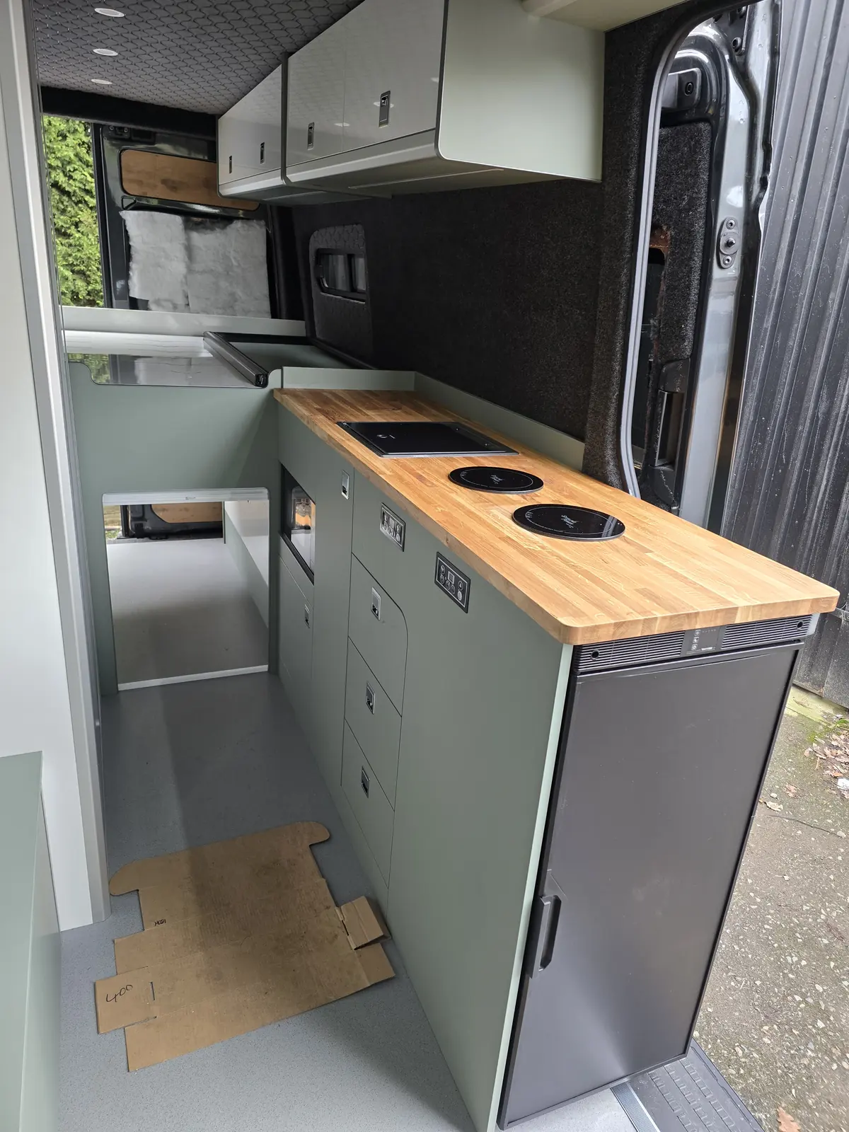 Green kitchen pod with an oak worktop and hobs, by the sliding door